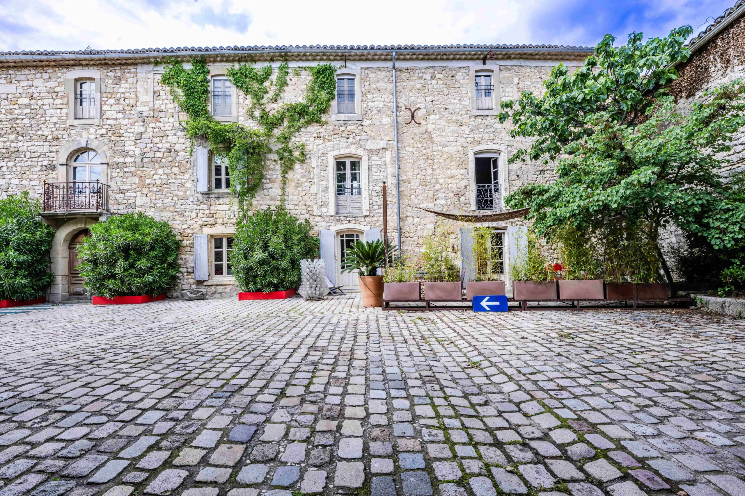 Façade en pierre avec lierre, cour pavée.