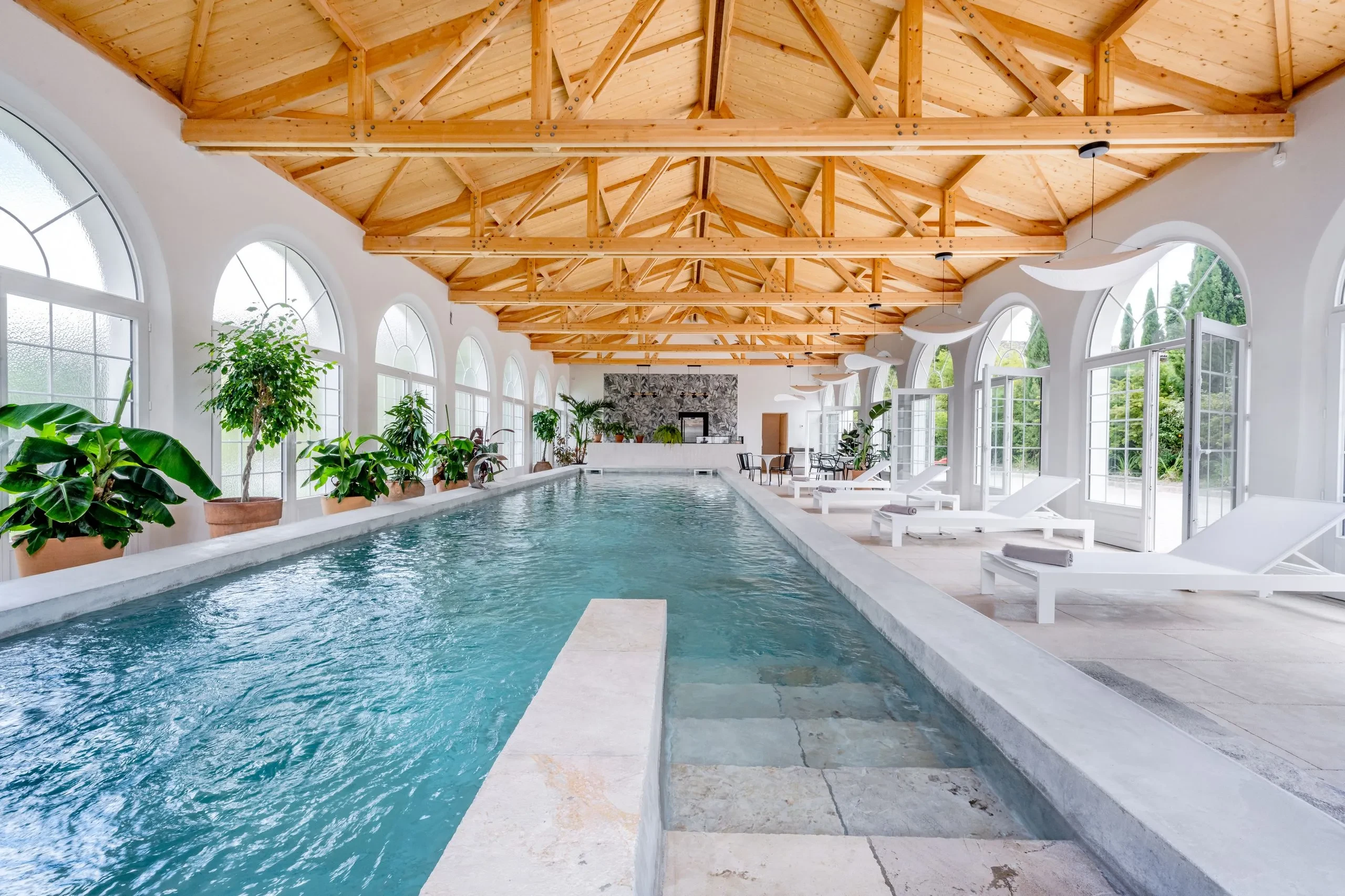 Piscine intérieure avec chaises longues et plantes vertes.