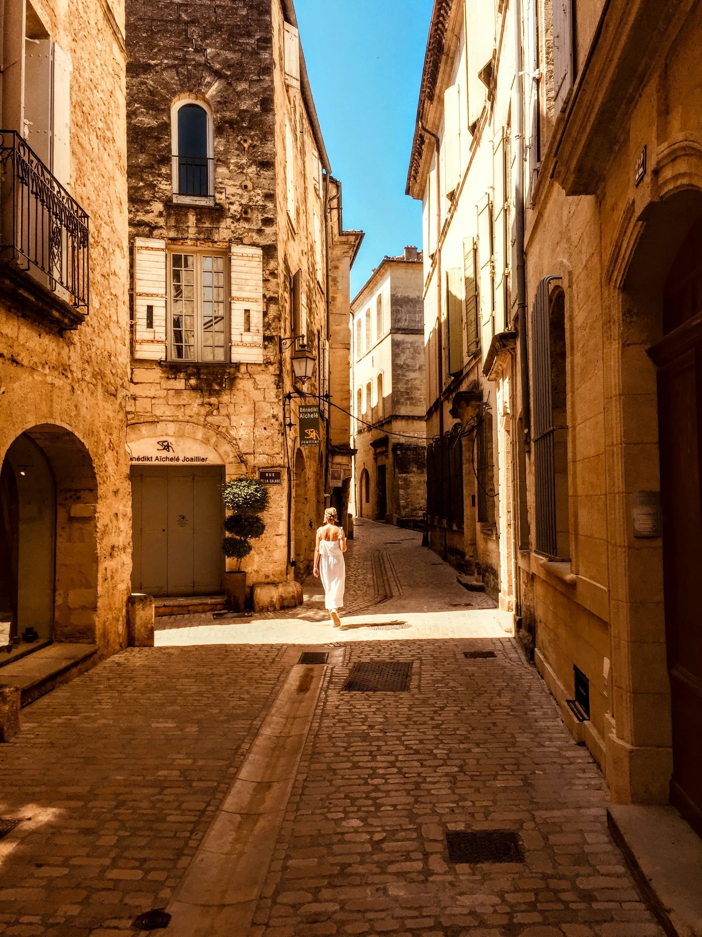 Femme marchant dans une ruelle historique ensoleillée.